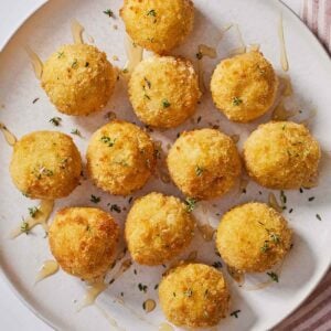 Overhead view of a plate of air fryer goat cheese balls with honey and fresh herbs on top.