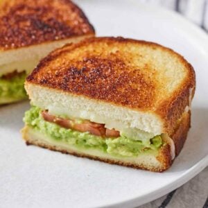An avocado grilled cheese cut in half with the focus on one half.