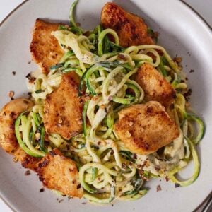 Overhead view of a plate of chicken Alfredo with zucchini noodles with red chili flakes on top.