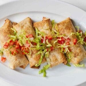 Overhead view of a platter with four chicken chimichanga with shredded lettuce and diced tomatoes on top.