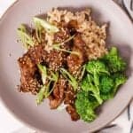A plate with rice, broccoli, orange beef, and scallions.