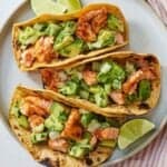 Overhead view of three salmon tacos on a plate with lime wedges around it.