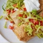 Pinterest graphic of two chicken chimichangas with guacamole, sour cream, shredded lettuce, and diced tomatoes.