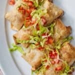 Pinterest graphic of an overhead view of a platter of four chicken chimichangas with shredded lettuce and diced tomatoes.