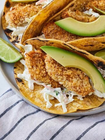 A plate with air fryer fish tacos with a focus on the crispy fish filling with sliced avocado and coleslaw.