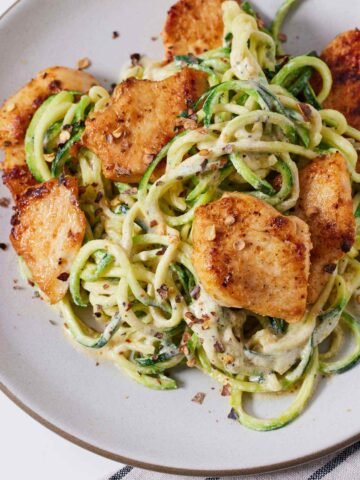 Overhead view of a plate of chicken Alfredo with zucchini noodles with red pepper flakes on top.