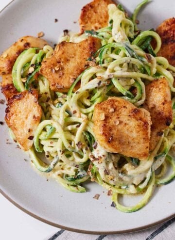 Overhead view of a plate of chicken Alfredo with zucchini noodles with red pepper flakes on top.