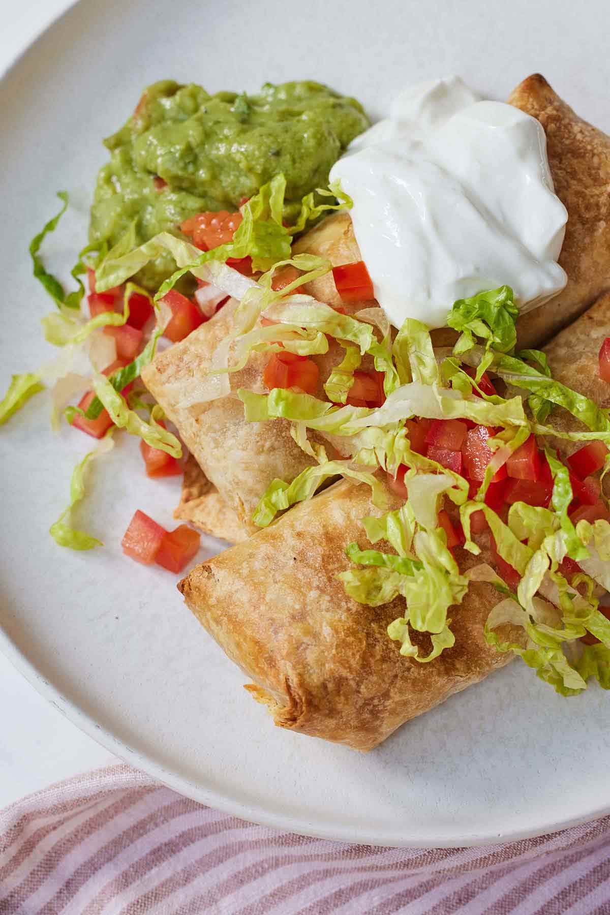 A plate of chicken chimichanga with guacamole beside it and sour cream on top with lettuce and tomatoes.