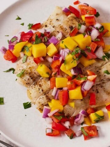 Overhead view of mango salsa on top of freshly grilled halibut on a plate.