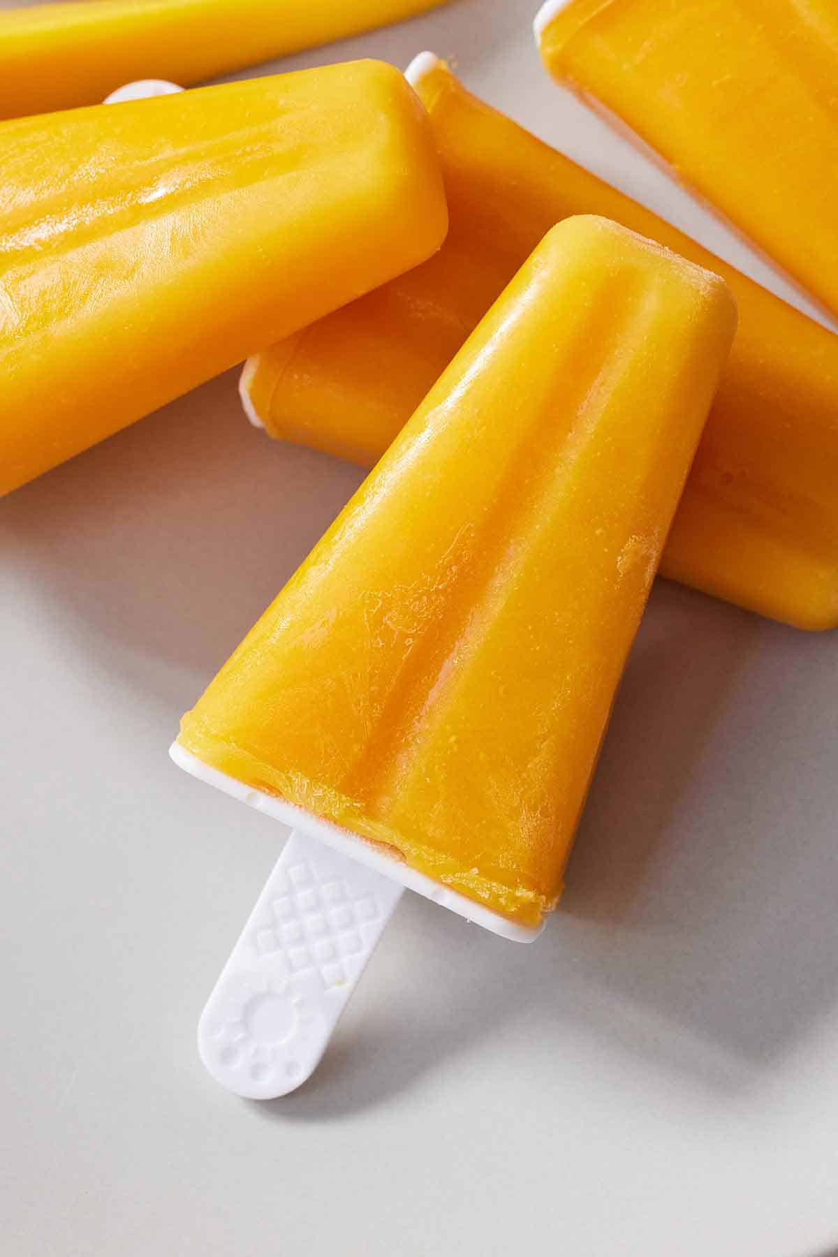 A mango popsicle leaning against other popsicles.