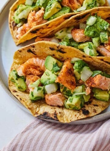 Overhead view of a plate of three salmon tacos.