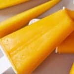 Pinterest graphic of a close view of a mango popsicle by two slices of freshly cut mango.