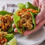Pinterest graphic of a half lifting up a Thai chicken lettuce wrap from a plate.