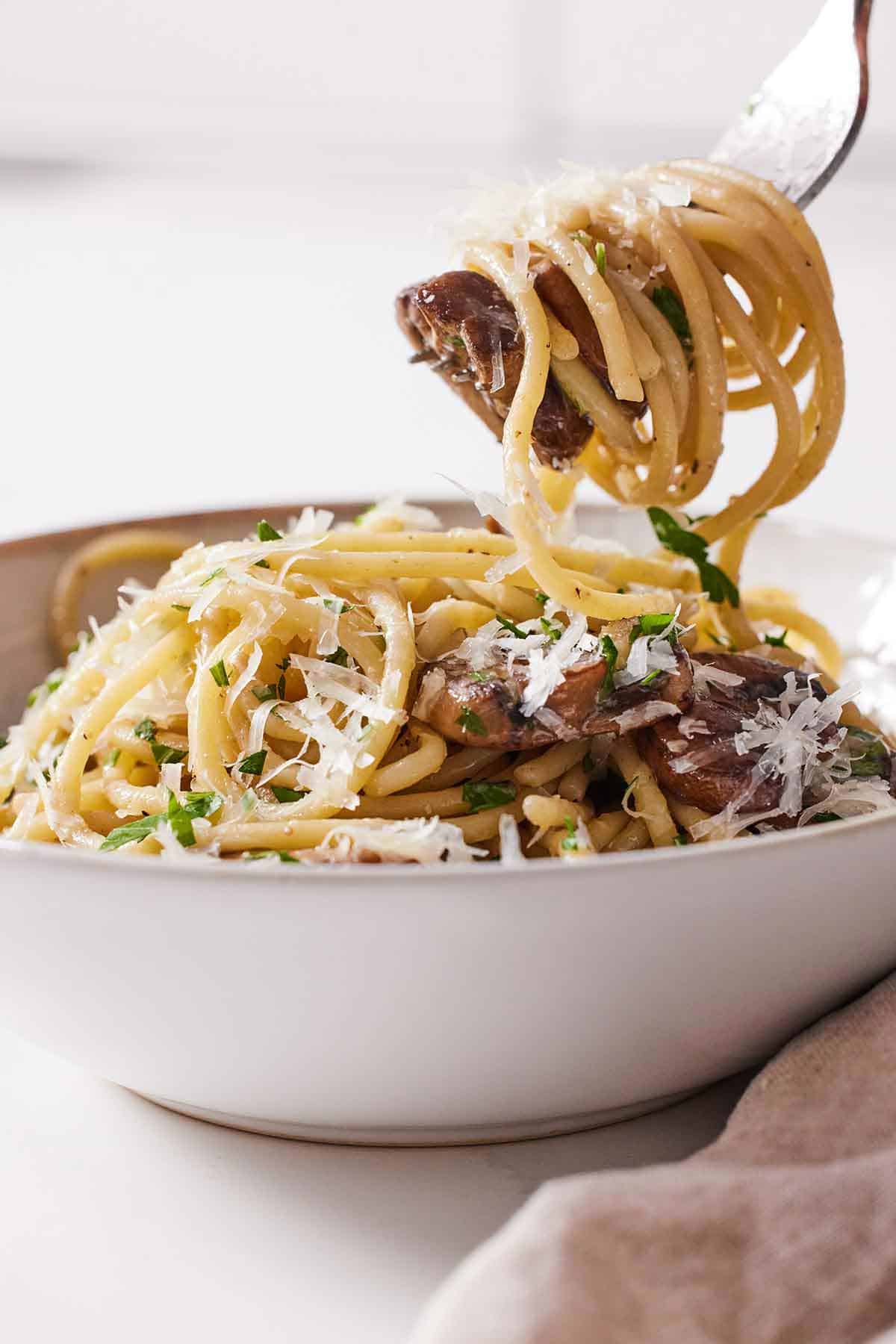 A fork wth garlic mushroom pasta twirled on it, lifted from a bowl of pasta.