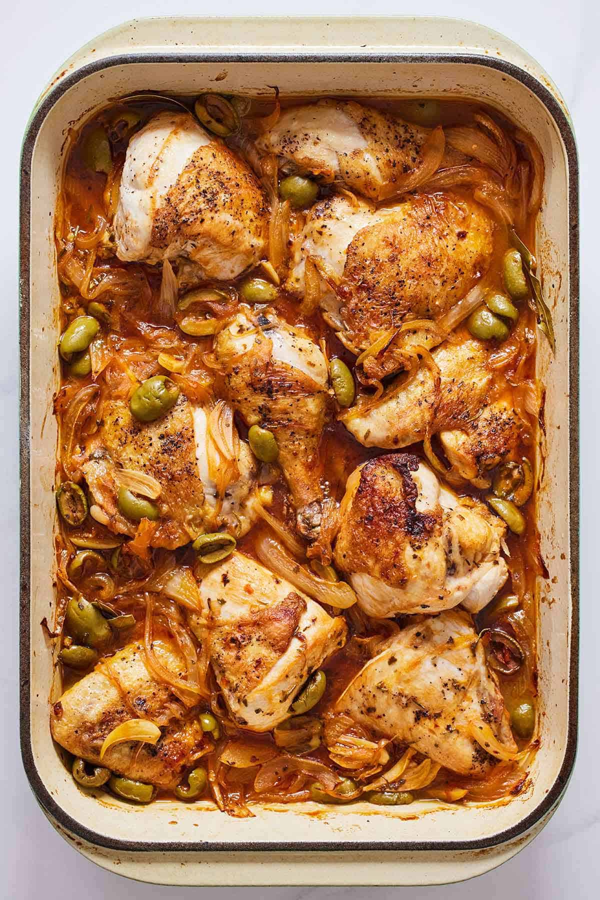 Overhead view of a baking dish with saucy braised chicken thighs with their skins on.