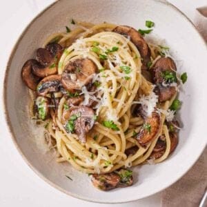 Overhead view of garlic mushroom pasta in a bowl with fresh parsley and parmesan on top.