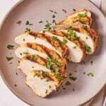 Overhead view of a plate with Mediterranean grilled chicken, sliced and garnished with parsley.