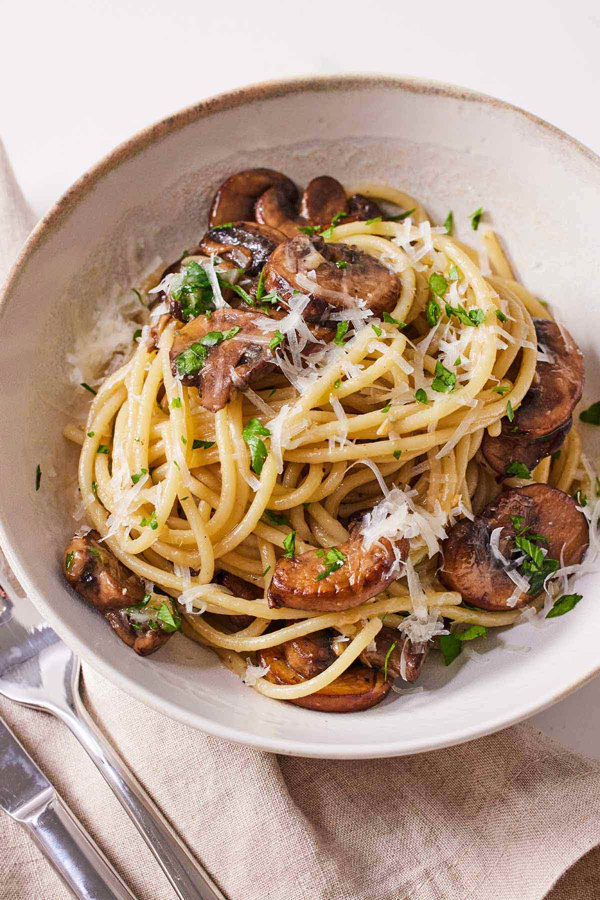 A bowl of garlic mushroom pasta with fresh parsley and grated parmesan on top.
