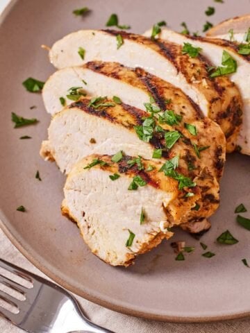 A plate with a Mediterranean grilled chicken breast sliced with fresh parsley on top.
