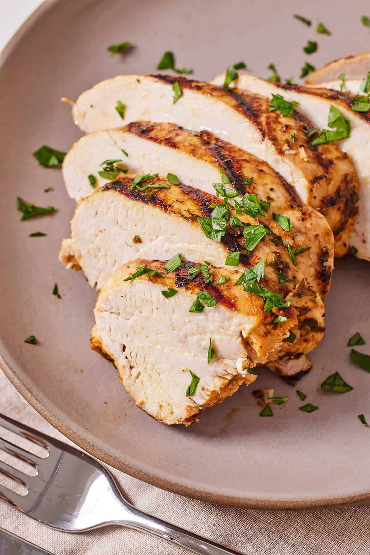 A plate with a Mediterranean grilled chicken breast sliced with fresh parsley on top.