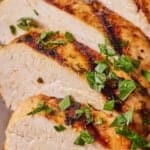 Pinterest graphic of a close up view of sliced Mediterranean grilled chicken breasts with chopped parsley on top.