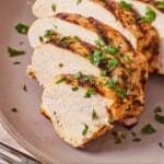 Pinterest graphic of a sliced grilled Mediterranean chicken breast on a pink plate with parsley on top.