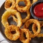 Pinterest graphic of a plate with multiple different sized air fryer onion rings with ketchup on the side.