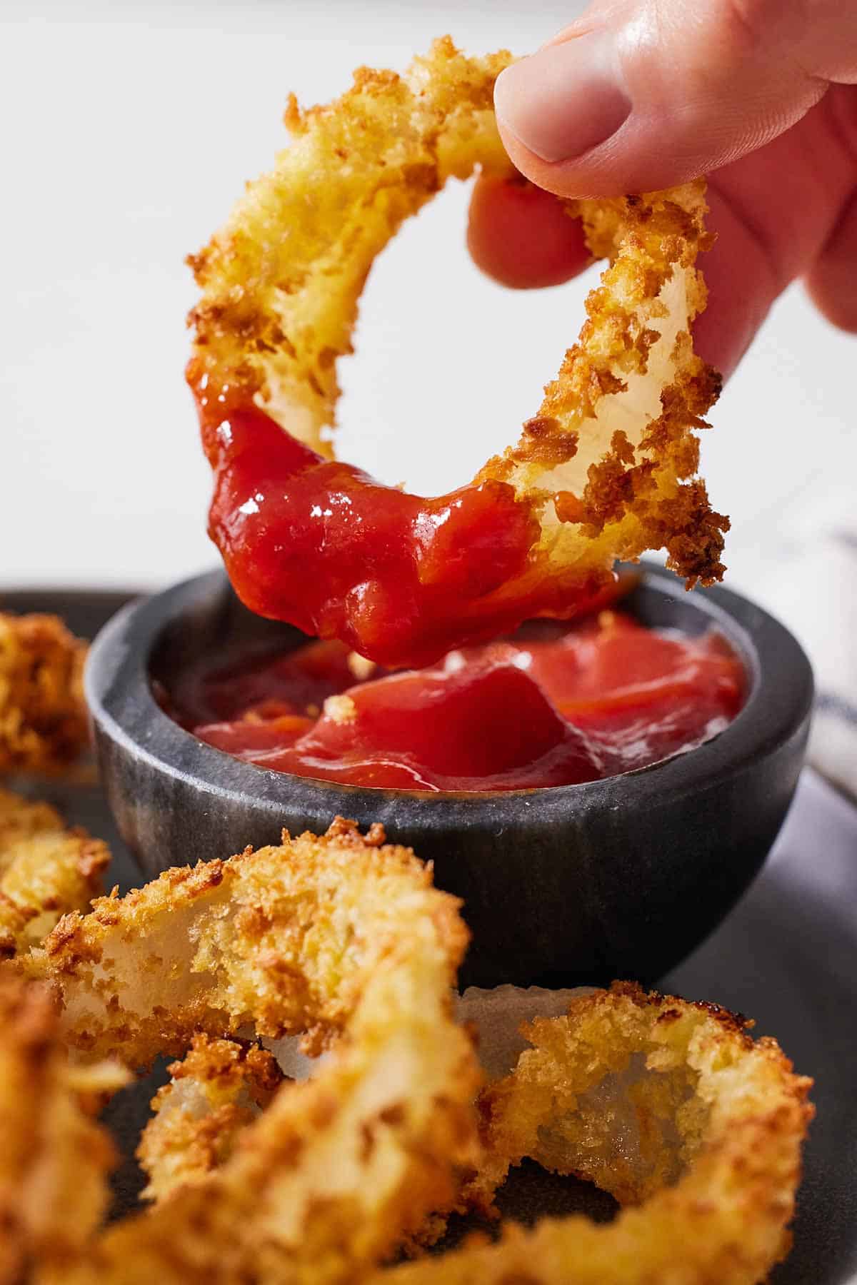 An air fryer onion ring dipped into a pinch bowl of ketchup.
