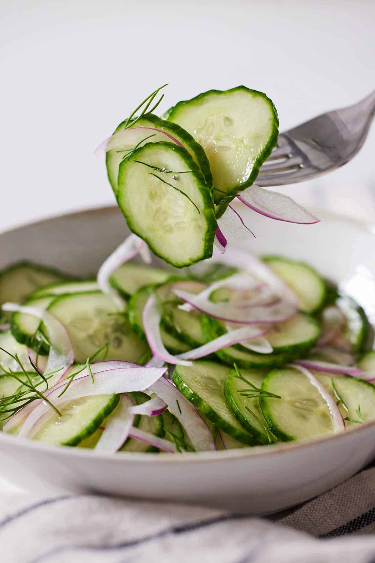 A bowl of cucumber salad with a fork lifting
