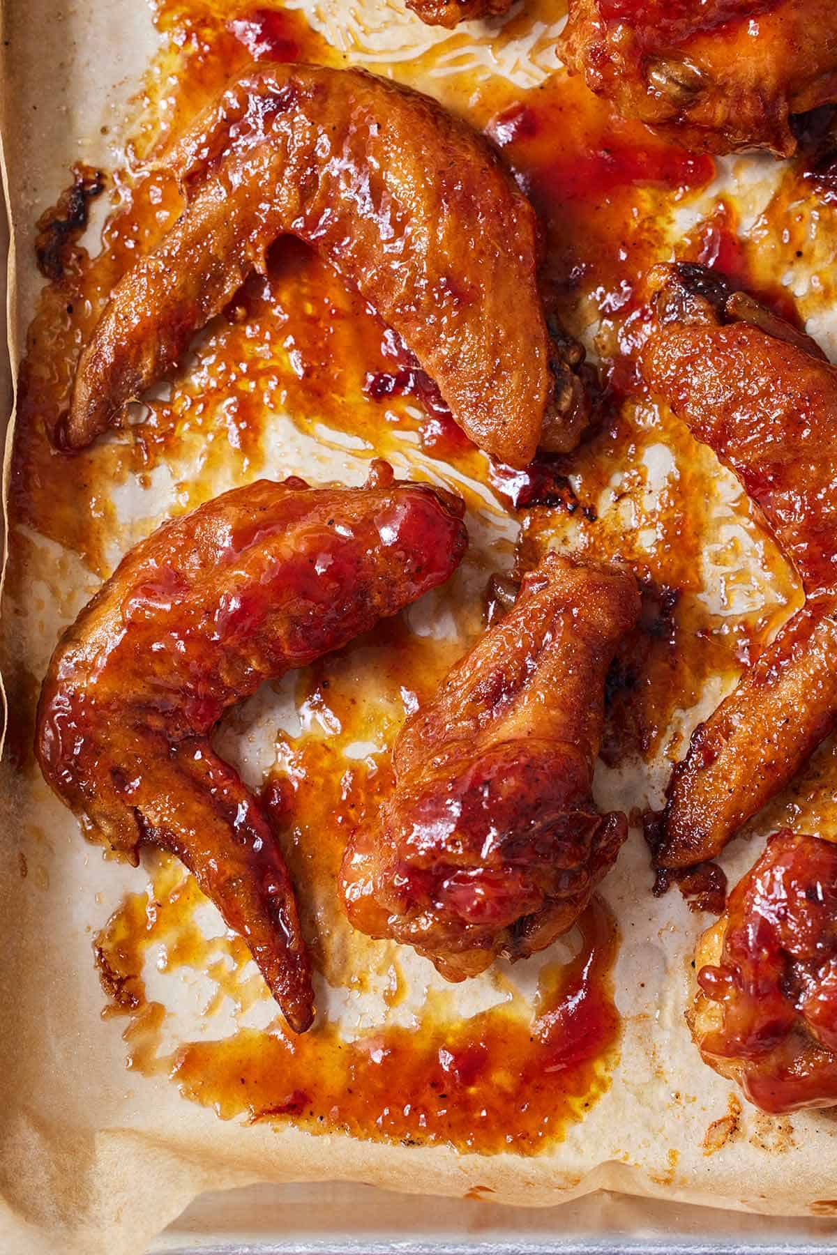Overhead view of multiple honey BBQ wings on a parchment lined sheet pan.