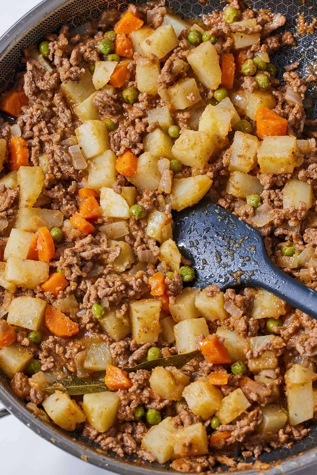 A skillet of Mexican picadillo with a rubber spatula tucked into the middle of the pan.