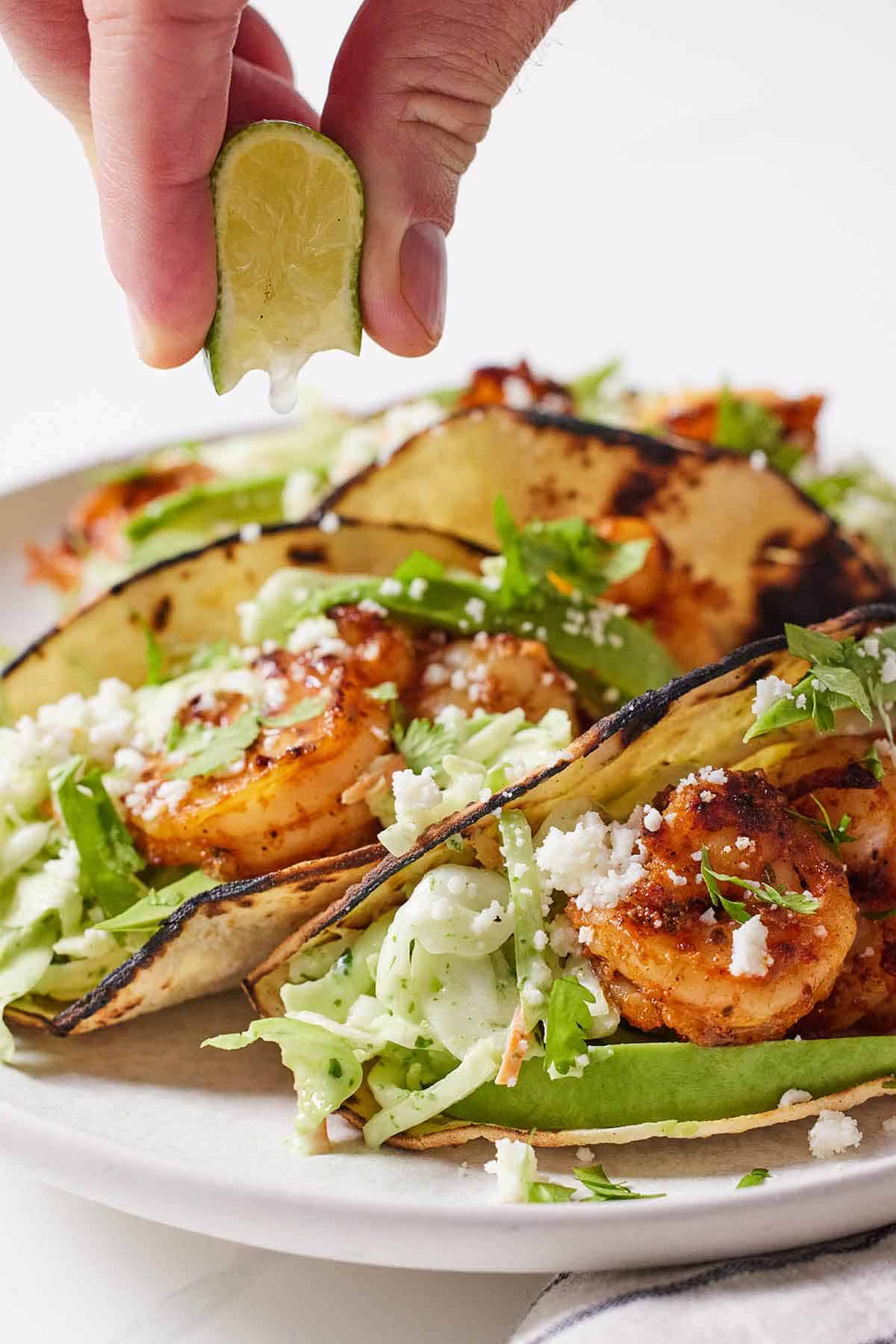 A plate of shrimp tacos with a lime wedge squeezed over top.