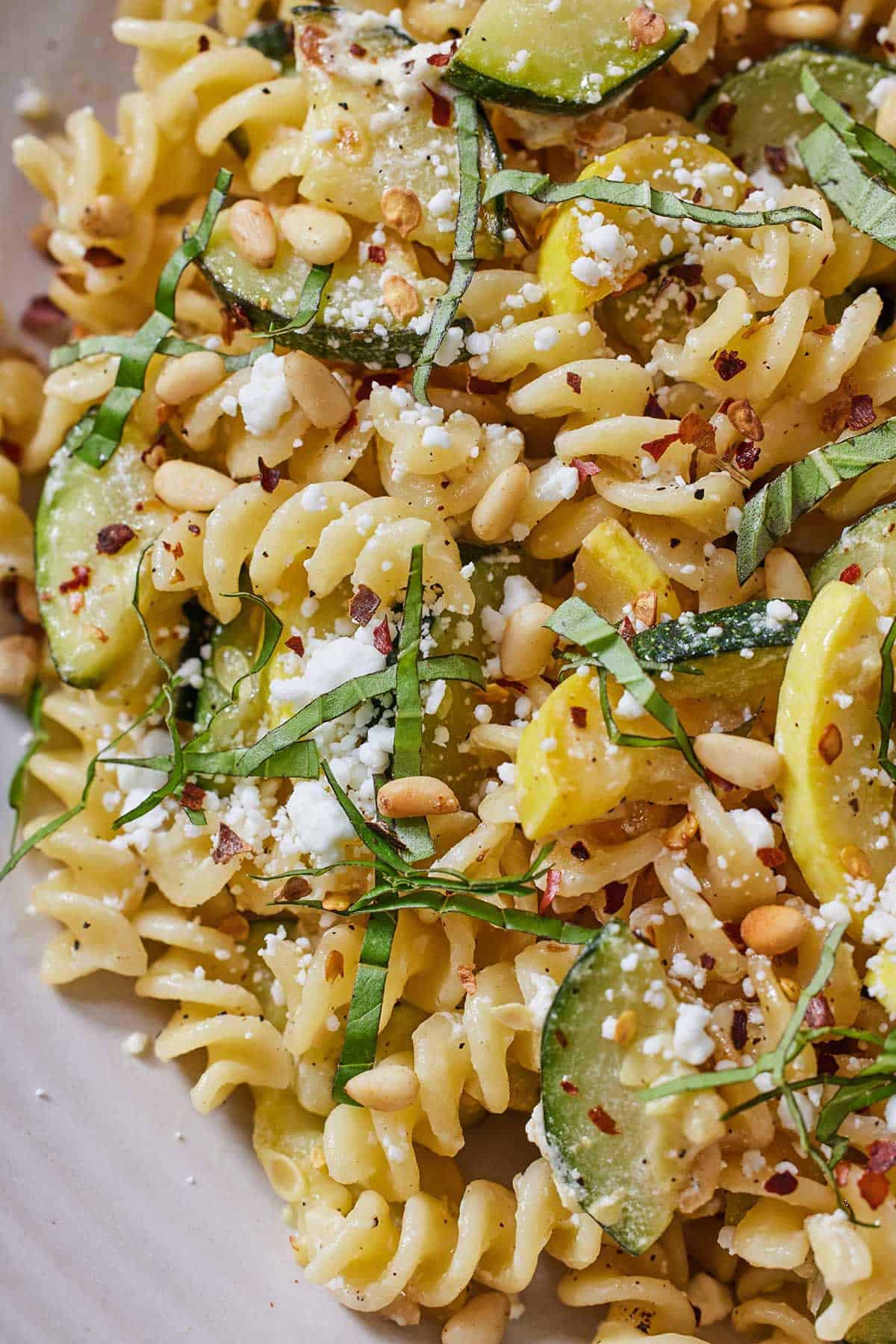 Close up view of summer squash pasta with red chili flakes and ribboned basil on top.