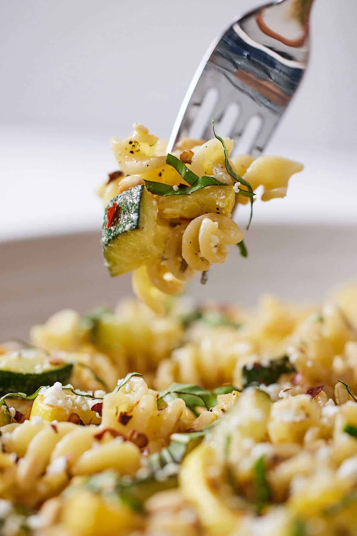 A forkful of summer squash pasta lifted from a bowl of pasta.