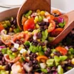 Pinterest graphic of large wooden spoons scooping up black bean salad from a bowl.