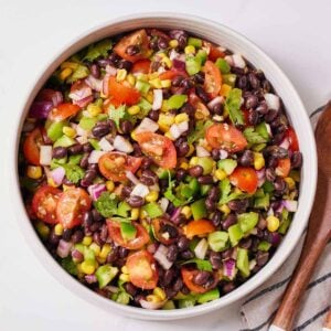 Overhead view of a bowl of black bean salad with a large wooden spoon on the side.