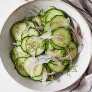 Overhead view of a bowl of cucumber salad with fresh dill on top.