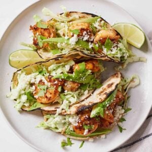 Overhead view of three shrimp tacos with lime wedges around it and cotija cheese sprinkled on top.