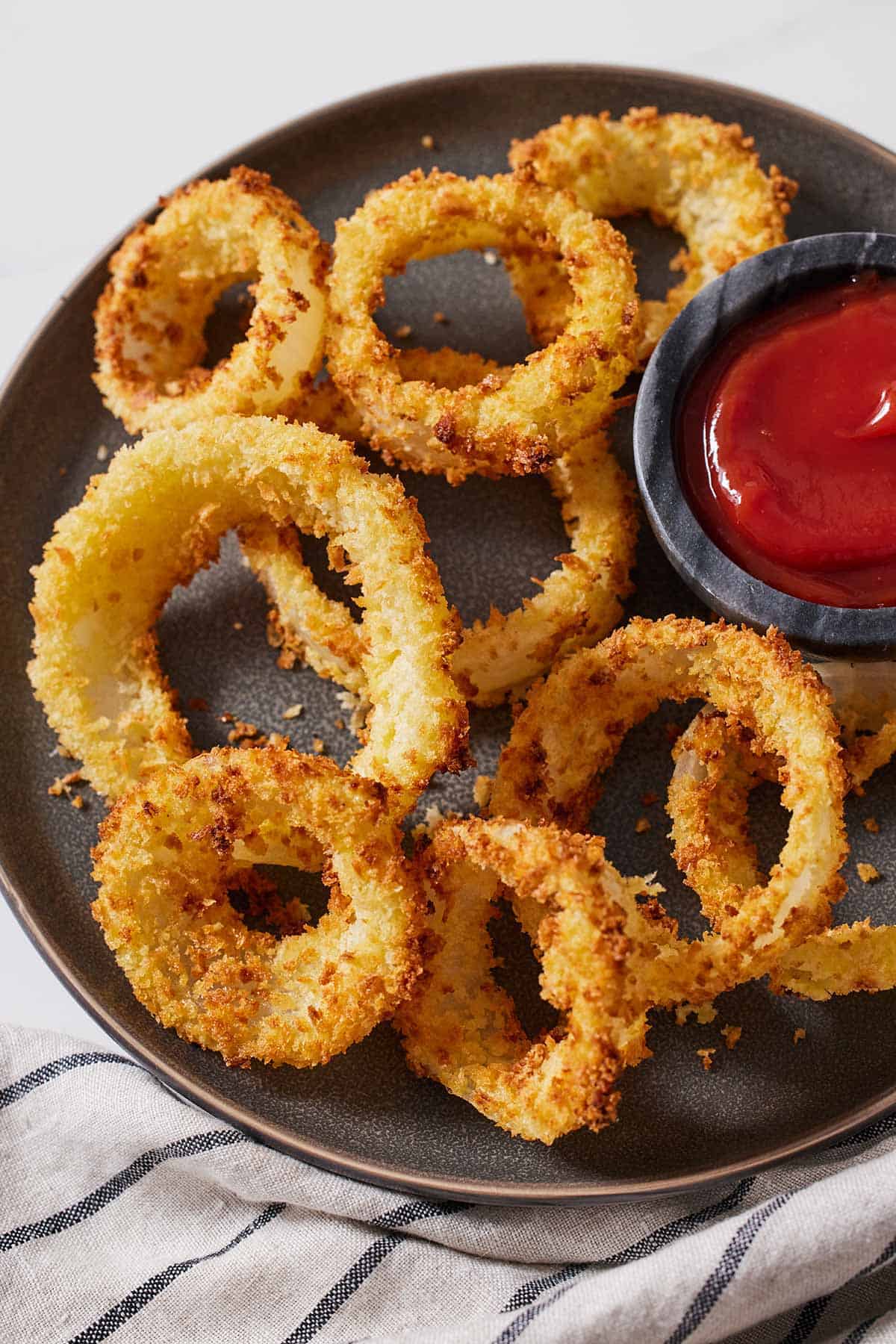 A plate with multiple air fryer onion rings by a bowl of ketchup.