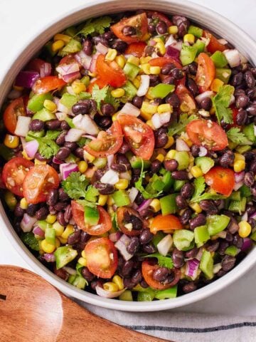 A bowl of black bean salad with wooden serving spoons on the side.