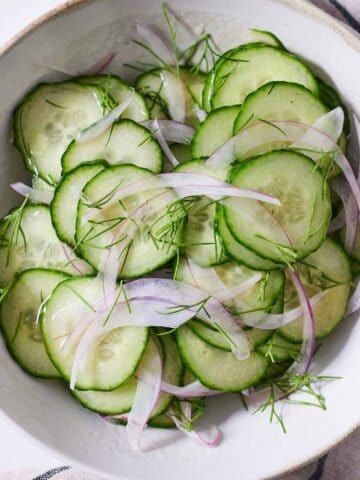 A plate of cucumber salad with fresh dill on top.