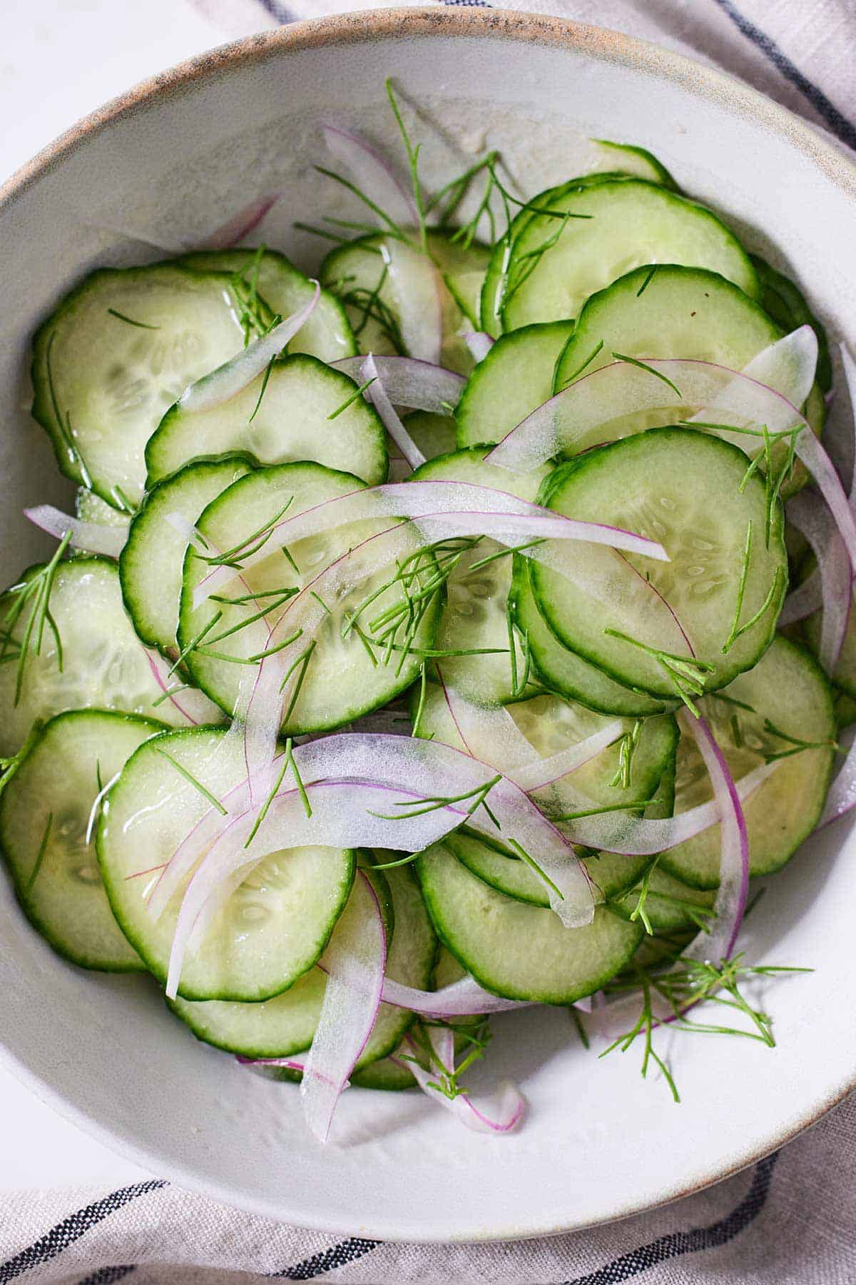 A plate of cucumber salad with fresh dill on top.