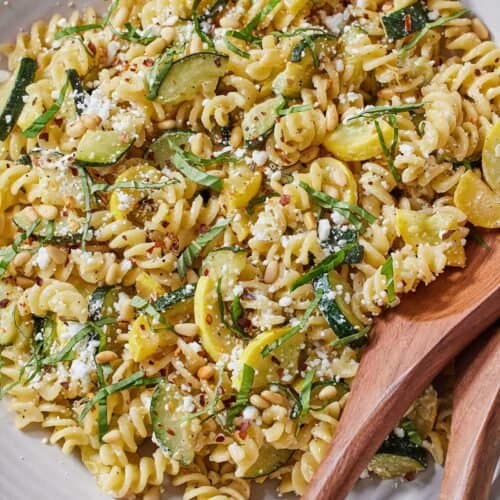 A large plate of summer squash pasta with wooden serving utensils tucked into the side.