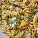Pinterest graphic of a close up view of summer squash pasta with basil, red chili flakes, and crumbled cheese on top.