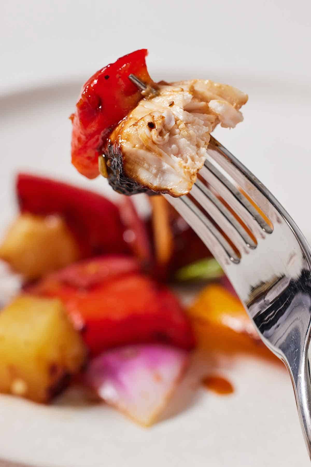 A fork with a piece of chicken and bell pepper.