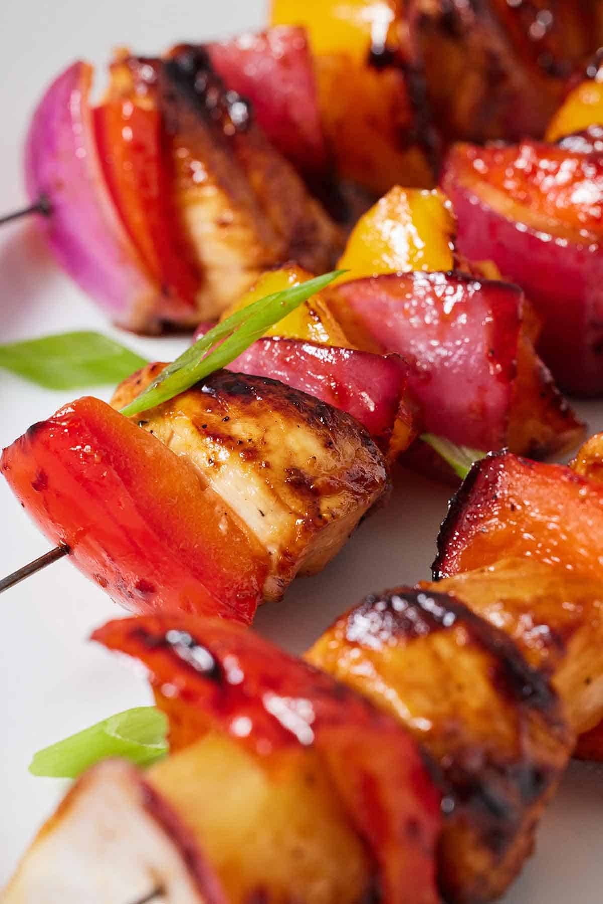 Close up with three Hawaiian chicken skewers with some green onions on top.