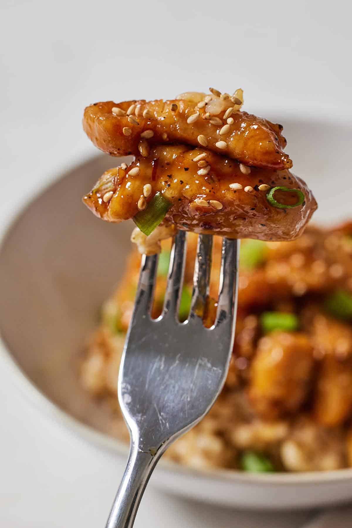 A fork with two pieces of honey garlic chicken bites on top.