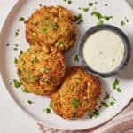 Overhead view of a plate with three air fryer crab cakes and dip on the side.