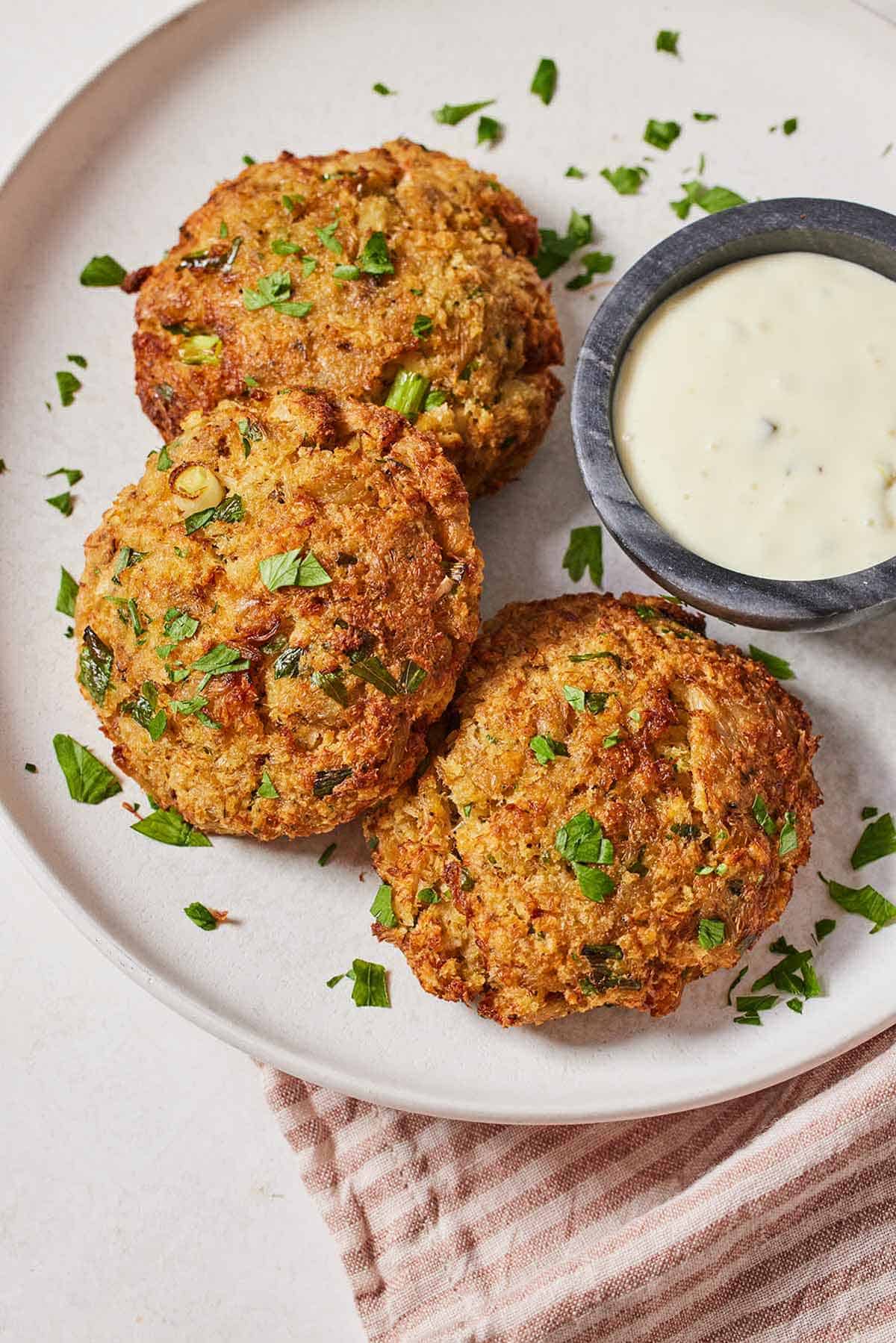 Overhead view of a plate of three air fryer crab cakes with a dip on the side.