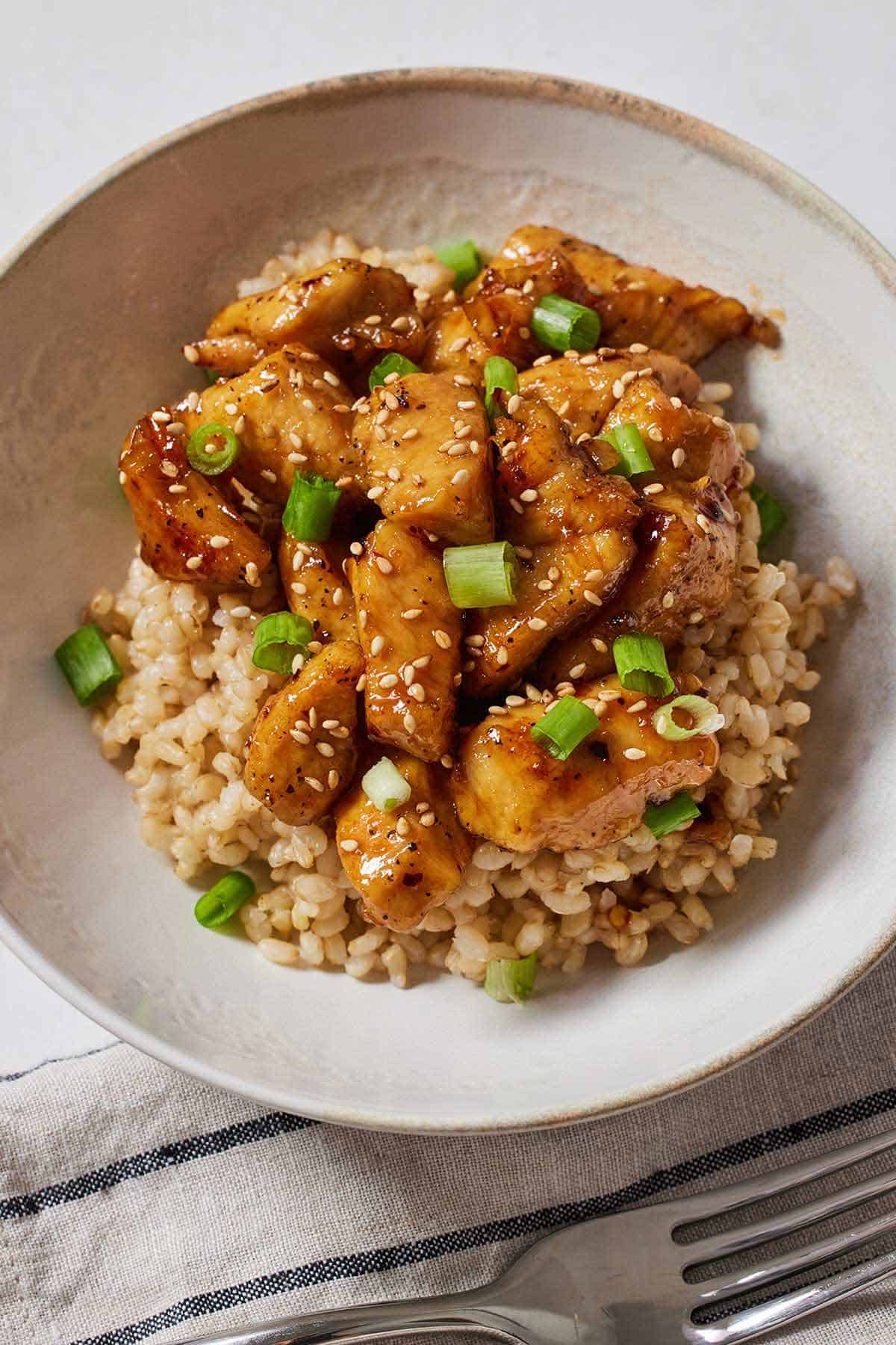 A bowl of rice with honey garlic chicken bites on top.
